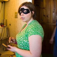Woman wearing a black caper mask while putting on makeup